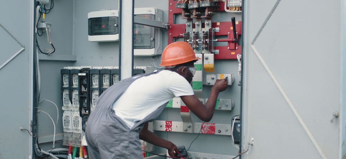african-american-man-in-overalls-safety-helmet-and-glasses-working-on-switchgear-at-so-SBI-351269919
